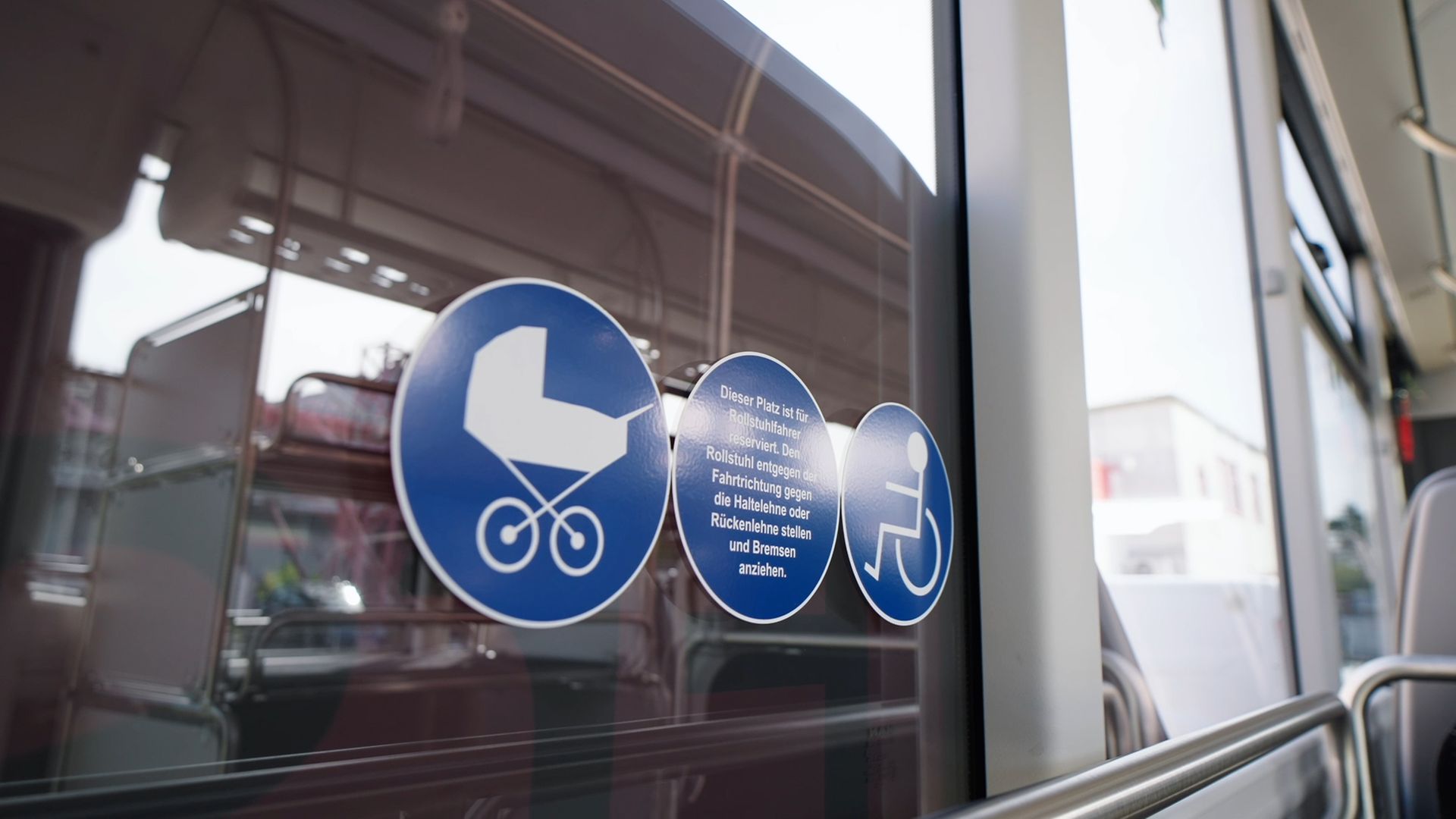 Zu sehen sind blaue runde Aufkleber auf der Scheibe eines Busses, die auf barrierefreie Plätze hinweisen.