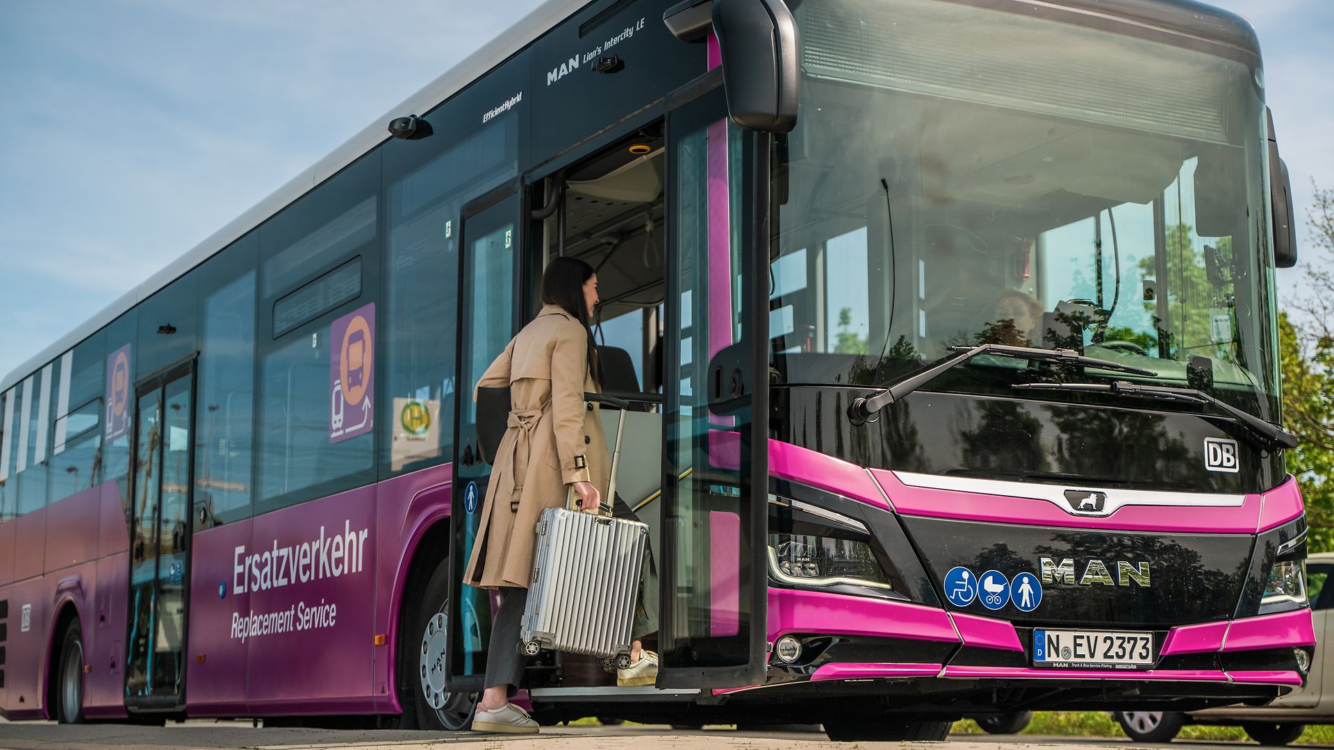 Zu sehen ist eine Frau mit Rollkoffer, die vorn in einen violetten Ersatzverkehr-Bus einsteigt.