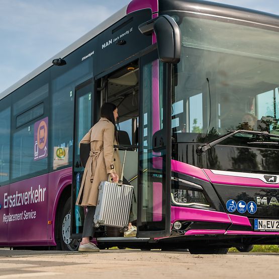 Zu sehen ist eine Frau mit Rollkoffer, die vorn in einen violetten Ersatzverkehr-Bus einsteigt.